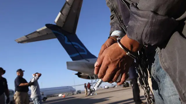 Um imigrante guatemalteco indocumentado espera, algemado por ser acusado de um crime, se prepara para embarcar num voo de deportação para a Cidade da Guatemala, em 24 de junho de 2011 em Mesa, no Arizona (Foto de John Moore/Getty Images)