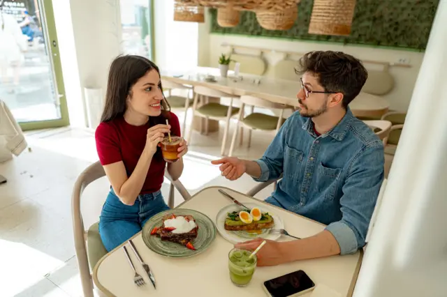 Una pareja millenial comiendo tostadas de aguacate en una cafetería moderna.