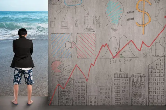 Hombre vestido de ejecutivo arriba y traje de baño abajo mirando a la playa al lado de un muro con cuestiones comerciales.