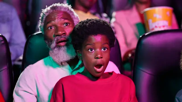 Idoso e jovem olhando assustados para a tela em uma sala de cinema
