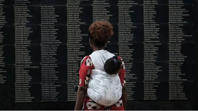 Umugore usoma urutonde rwa bamwe mu bashyinguye mu rwibutso rwa Jenoside rwa Kigali ruri ku Gisozi