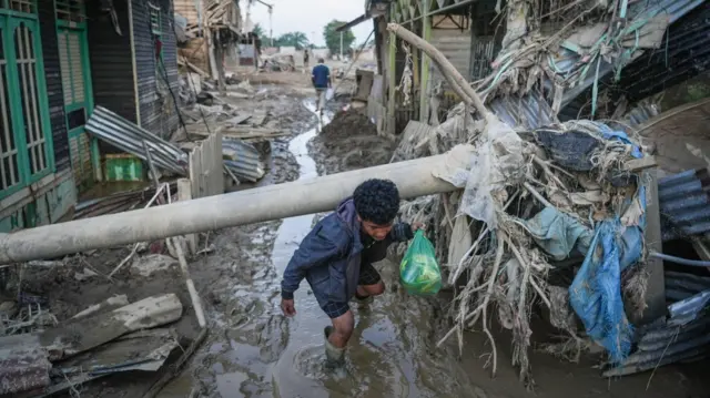 Warga merunduk melewati tiang listrik yang roboh akibat banjir bandang di Kuala Simpang, Kabupaten Aceh Tamiang, Aceh, Sabtu (6/12/2025).