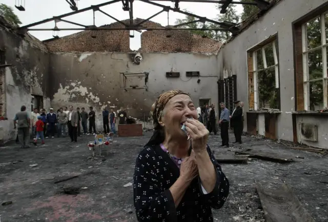 Mulher chorando dentro do ginásio destruído da escola dias após o cerco.