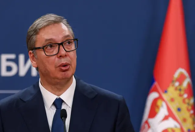 Вучич на тлі стіни та прапора Сербії