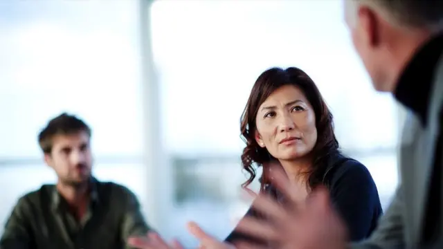 Une femme écoute un homme parler tandis qu'un autre homme regarde.