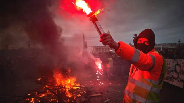 Protester stands with flare by fire during demonstrations in Paris