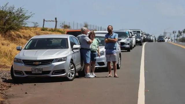 People wait on the side of the road to return to west Maui after wildfires driven by high winds were believed to have destroyed much of the historic town of Lahaina, in Kahului, Hawaii, U.S. August 9, 2023.