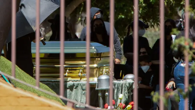 Золотой гроб и люди в масках на похоронах Эль Менчо. Фото сделано сквозь решетку ограды