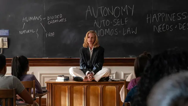 Кадр із фільму "Після полювання" - білява жінка сидить на викладацькому столі в аудиторії, схрестивши ноги