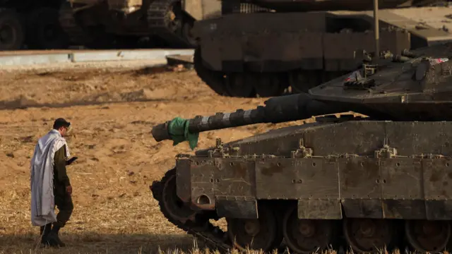 دبابة إسرائيلية في غزة يقف أمامها جندي إسرائيلي، الصورة التقطت نهاراً.