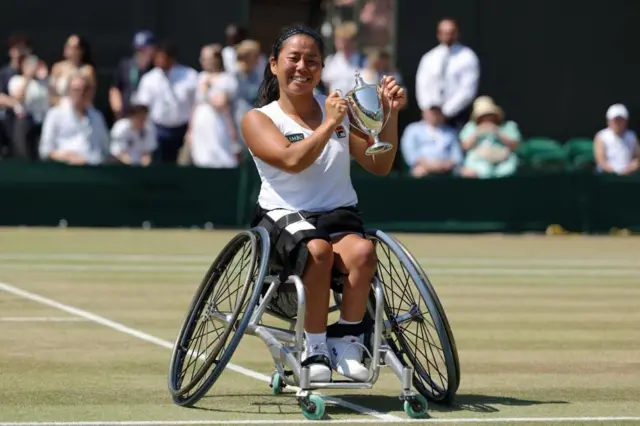 Tennis - Wimbledon - All England Lawn Tennis and Croquet Club, London, Britain - July 11, 2026
Japan's Yui Kamiji poses with the trophy during the presentation ceremony after winning her ladies' wheelchair singles final match REUTERS/Marko Djurica
車いすに座った白いウェアの上地がコート上で、両手でトロフィーを体の前で持っている