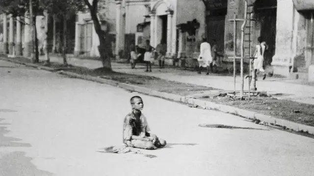 দশ বছর বয়সী একটি শিশু রাস্তায় বসে আছে, পাশ দিয়ে হেঁটে যাচ্ছে পাঁচ-ছয় জন মানুষ