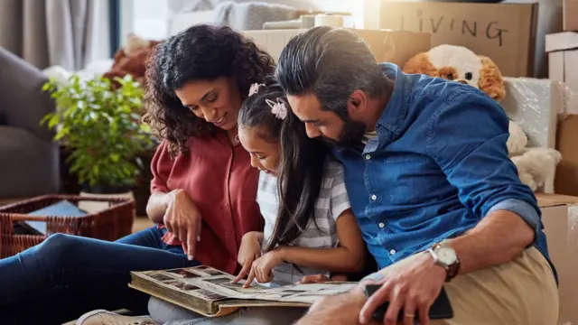 أب وأم وابنتاهما يجلسون على الأرض وينظرون بسعادة إلى ألبوم صور عائلية قديمة