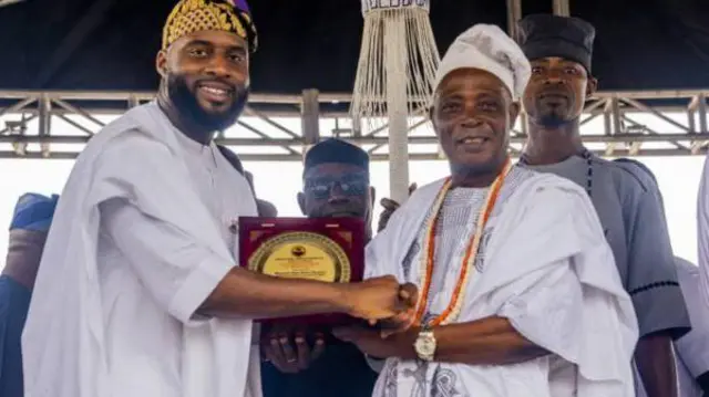 Abenugan ile igbimọ aṣofin ipinle Oyo, Ọnarebu Adebo Ogundoyin n gbe ami ẹyẹ kan fun ọba Rashidi Ladoja. Awọn mejeeji wọ agbada alawọ eeru, de fila, ti ọba Ladoja si fi ilẹkẹ meji sọrun