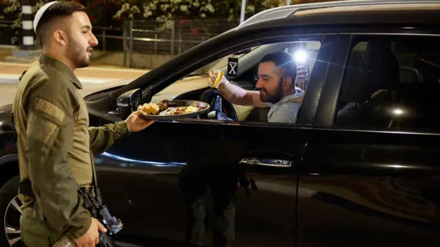 جندي إسرائيلي يوزع الطعام على شخص بعد أن قال الجيش الإسرائيلي إنه ربما قتل زعيم حماس يحيى السنوار، عند نقطة تفتيش في سديروت، إسرائيل