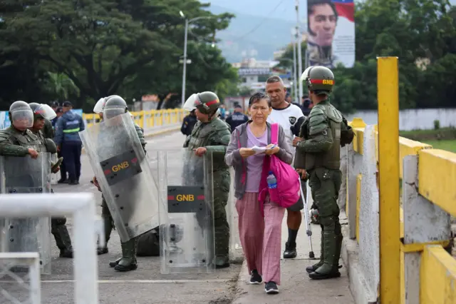 Una mujer atraviesa un cordón de agentes antimotines de la Guardia Nacional de Venezuela. 