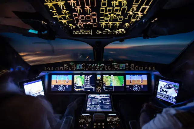 Vista de la cabina de mando de un avión y dos pilotos en ella.