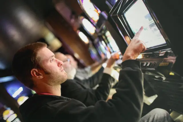 Homens sentados lado a lado em frente a máquinas de cassino