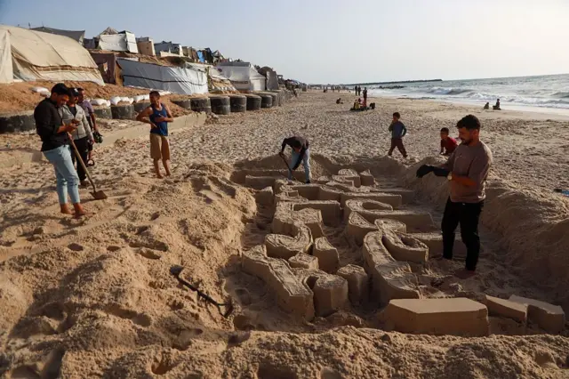 Seniman Palestina, Yezid Abu Jerad, membuat patung pasir bertuliskan 'Armada Kebebasan Gaza Memanggilmu' di pantai dekat sebuah pengungsian di Jalur Gaza, Selasa (19/05).