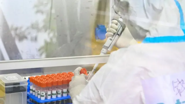 Una persona protegida con un traje especial manipula frascos de laboratorio.