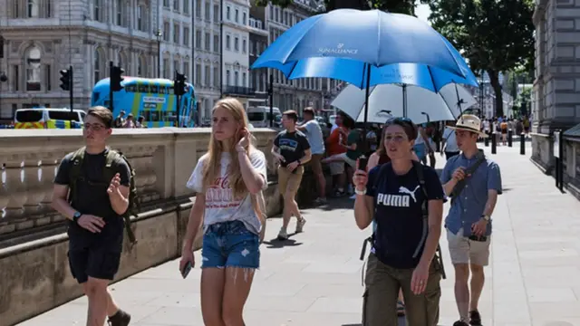A group walk down the street with an umbrella up to shade them from the sun