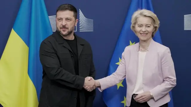Зеленский и фон дер Ляйен жмут друг другу руки на фоне флагов Украины и Евросоюза