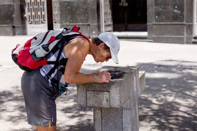 Жінка п'є воду із фонтана на вулиці 