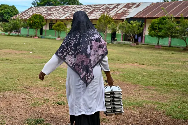 Seorang guru membawa nampan makanan ke kelasnya, yang disediakan oleh program makanan gratis pemerintah Indonesia, di sebuah sekolah dasar di Darul Kamal, provinsi Aceh pada 13 Oktober 2025