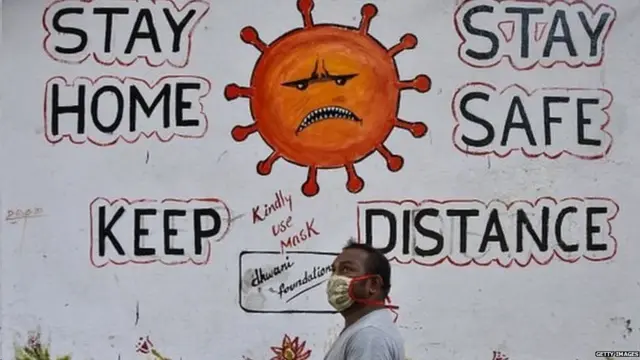 કોરોના સંબંધિત જાગૃતિ માટેના ભીંતચિત્ર પાસેથી પસાર થતો યુવક