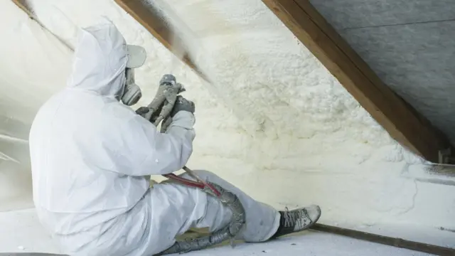 Un technicien pulvérise de la mousse de polyuréthane utilisée comme isolant de toiture (photo de stock)