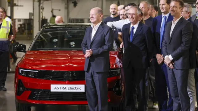 Olaf Scholz, Germany's chancellor, left, and Carlos Tavares, chief executive officer of Stellantis NV, second left, and Florian Huettl, chief executive officer of Opel Automobile GmbH, right, during 125th anniversary celebrations at the Opel Russelsheim Plant in Russelsheim, Germany, on Saturday, June 8, 2024. Stellantis NV and Mercedes-Benz Group AG are putting work on two electric-vehicle battery plants on hold and may pivot to manufacturing lower-cost cells in light of slowing demand for still-expensive EVs. Photographer: Alex Kraus/Bloomberg via Getty Images