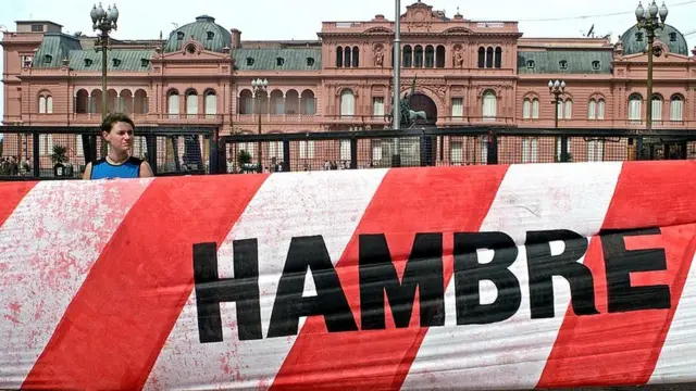 Un manifestante con una bandera que dice "hambre" con la Casa de Gobierno de Argentina a sus espaldas el 12 de diciembre de 2001 en Argentina.