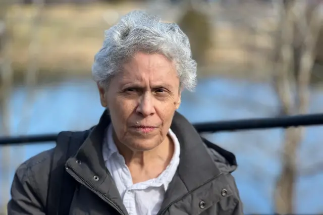 Dora María Téllez de casaco, em uma ponte sobre um curso d'água, em dia claro