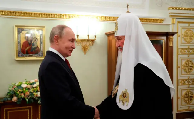 Путин пожимает руку патриарху Кириллу, оба улыбаются