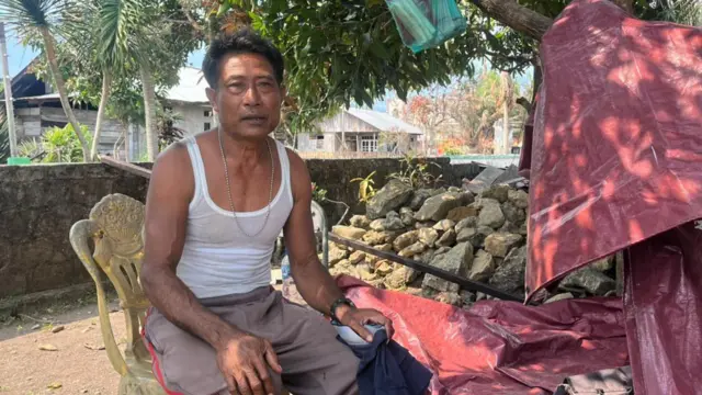 Warga Sibenpopo, Frans Anoano duduk di bawah pohon, dekat rumahnya yang rusak terbakar.