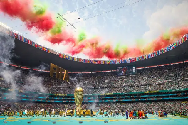 Imagem do evento de abertura da Copa do Mundo, com torcida, jogadores e taça gigante
