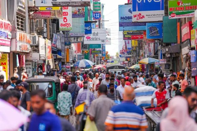 ජනාකීර්ණ කොළඹ නගරයේ වීදියක මිනිසුන් යන එන අයුරු
