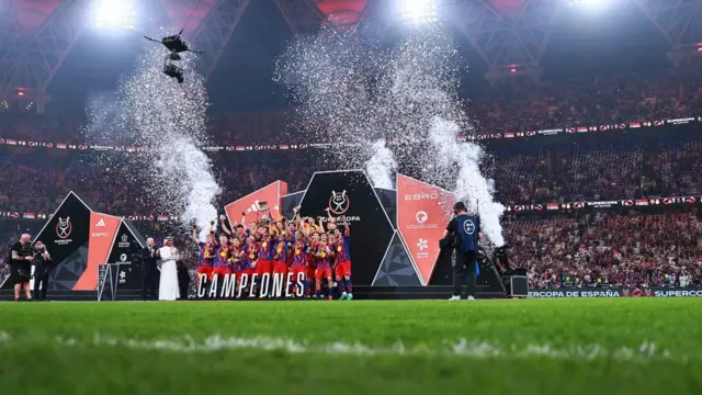 عکسی که شکوه ورزشگاه را هنگام بلند بردن جام توسط بارسلونا نشان میدهد. ورزشگاه پر از تماشاگر است.