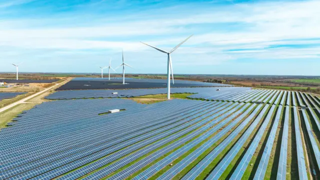 Campo de paineis solares com algumas turbinas eólicas