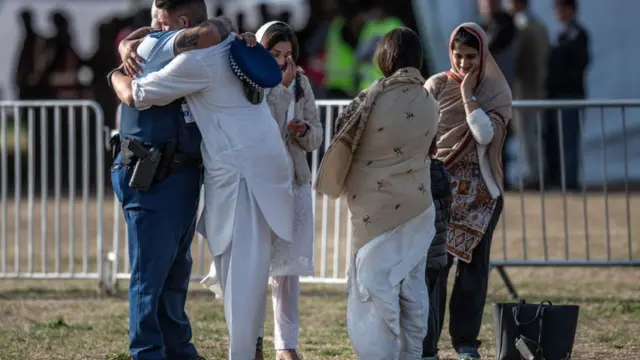 شرطي يحتضن أحد المعزين بينما ثلاثة نسوة يقفن متأثرات بالمشهد الجنائزي لضحايا الهجوم على مسجدين في نيوزيلندا