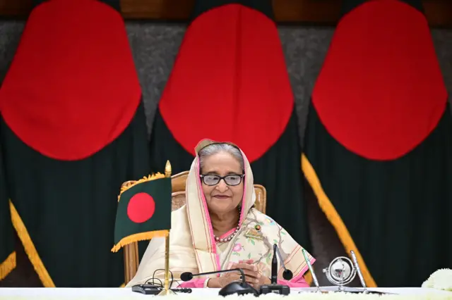 Bangladesh's Prime Minister Sheikh Hasina looks down at a table with microphones on it and a small Bangladeshi flag, as she attends the bilateral agreement signing ceremony in Dhaka on April 23, 2024.