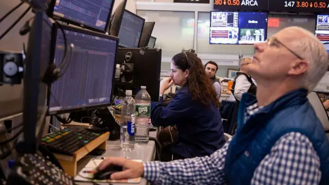 የአክስዮን ገበያ ውስጥ የሚሰሩ ሰዎች ኮምፒውተር ፊት ለፊት ቁጭ ብለው