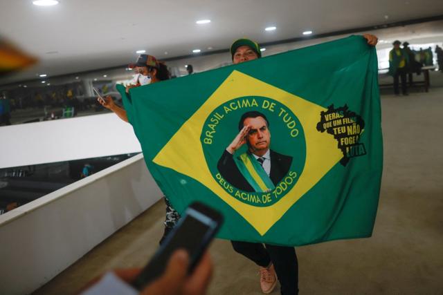 Pessoa dentrodinheiro com apostasprédio público com bandeira do Brasil alterada, mostrando fotodinheiro com apostasBolsonaro no centro