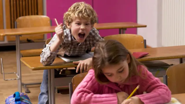Menino gritando atrás de uma colega de classe em sala de aula