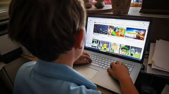 تصویر یک کودک که در مقابل لپ‌تاش نشسته او در حال تماشای ویدویوهای فوتبال در یوتیوب است. روی کودک به سمت صفحه کمپویتر و پشتش به سمت دوربین است. 