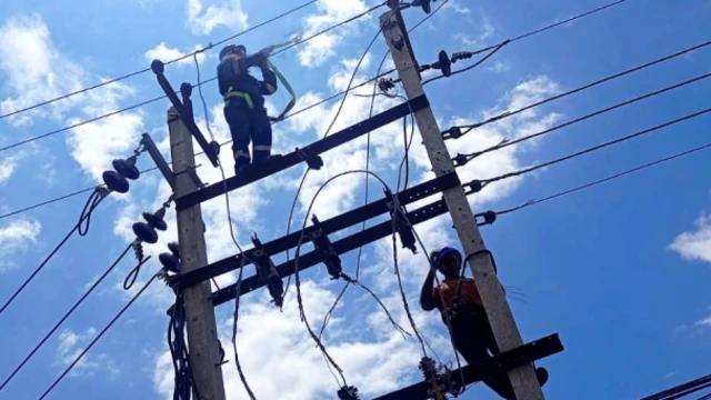 विद्युत् पोलहरू मर्मत गर्दै नेपाल विद्युत् प्राधिकरणका एक कर्मचारी, पृष्ठभूमिमा नीलो आकाश र सेता बादल 