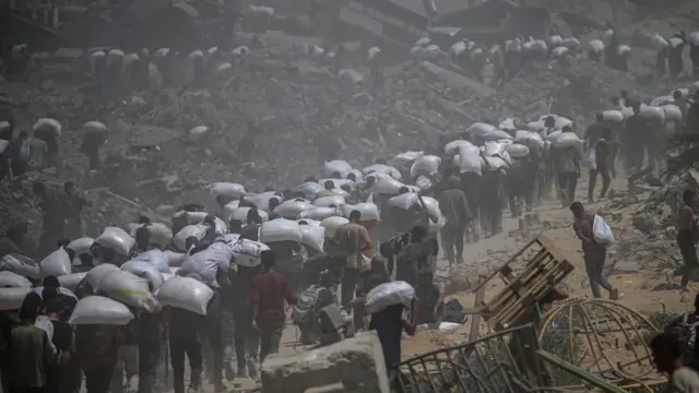 فلسطينيون نازحون يحملون أكياس دقيق قرب نقطة توزيع أغذية، شمال قطاع غزة