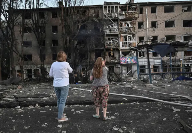 Mieszkańcy stoją przy budynku mieszkalnym trafionym w rosyjskim ataku dronów i rakiet w Zaporożu, 30 sierpnia 2025 r.