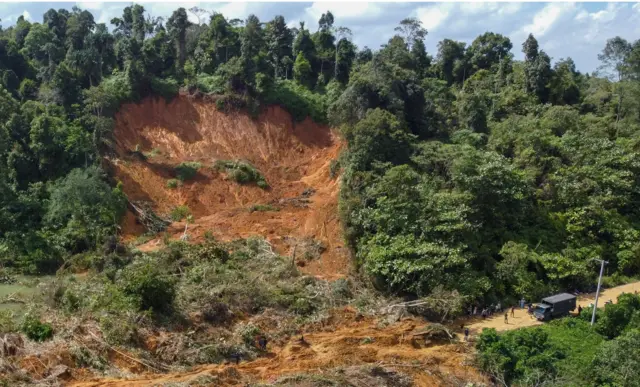 Foto udara warga melintasi material longsor berupa tanah, batu dan pohon yang menutupi jalan lintas antar Kabupaten Aceh Utara dan Kabupaten Bener Meriah di kecamatan Nisam Antara, Aceh Utara, Aceh, Minggu (30/11/2025).