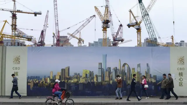 Personas caminando y pedaleando frente a una construcción.